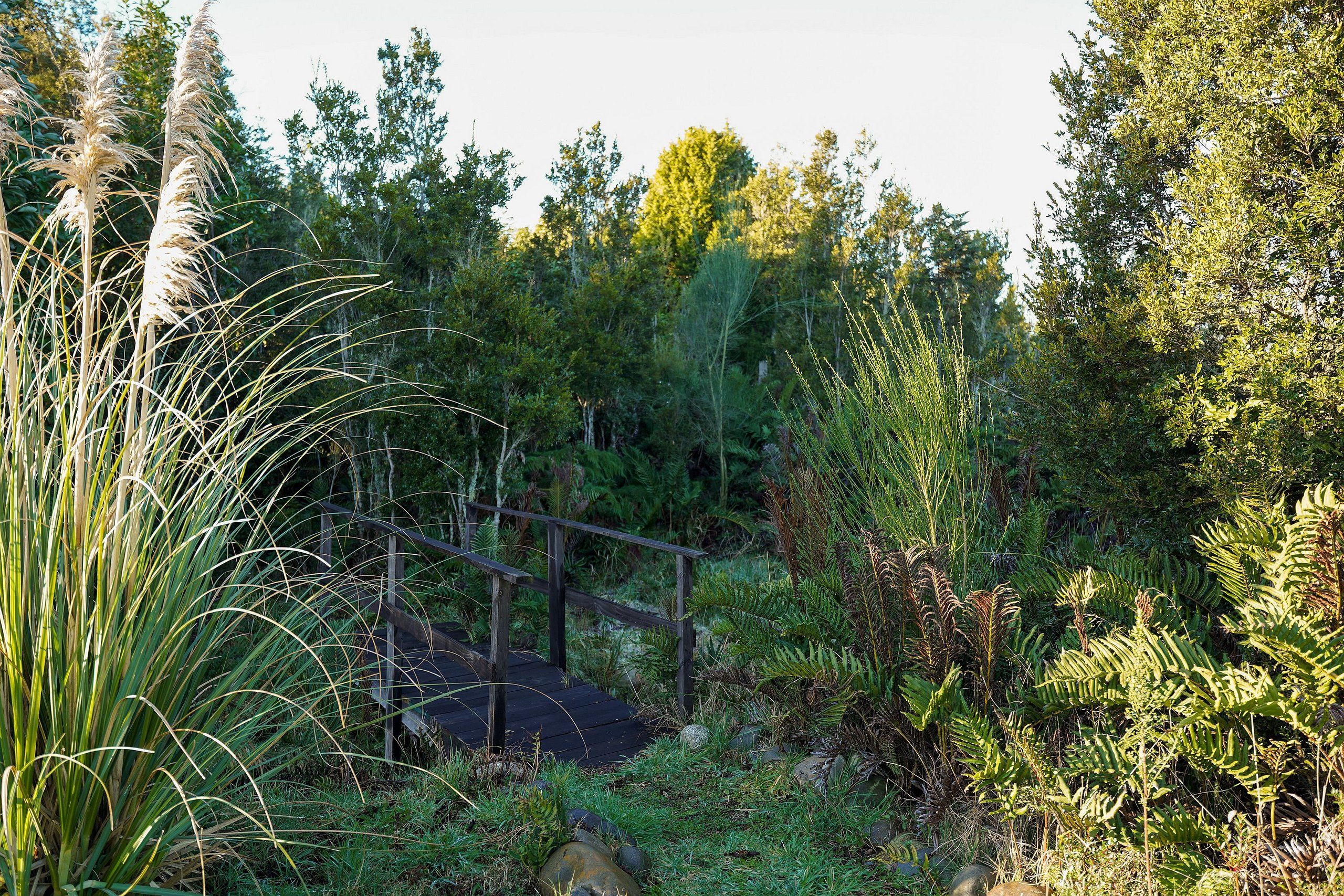 A wooden bridge over a rocky path surrounded by dense greenery and trees.