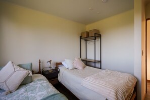 A bedroom with two single beds, a bedside table with a lamp, and a wall-mounted shelf with boxes. - Oceana Suites Altos de Neoalerce (Puerto Montt)
