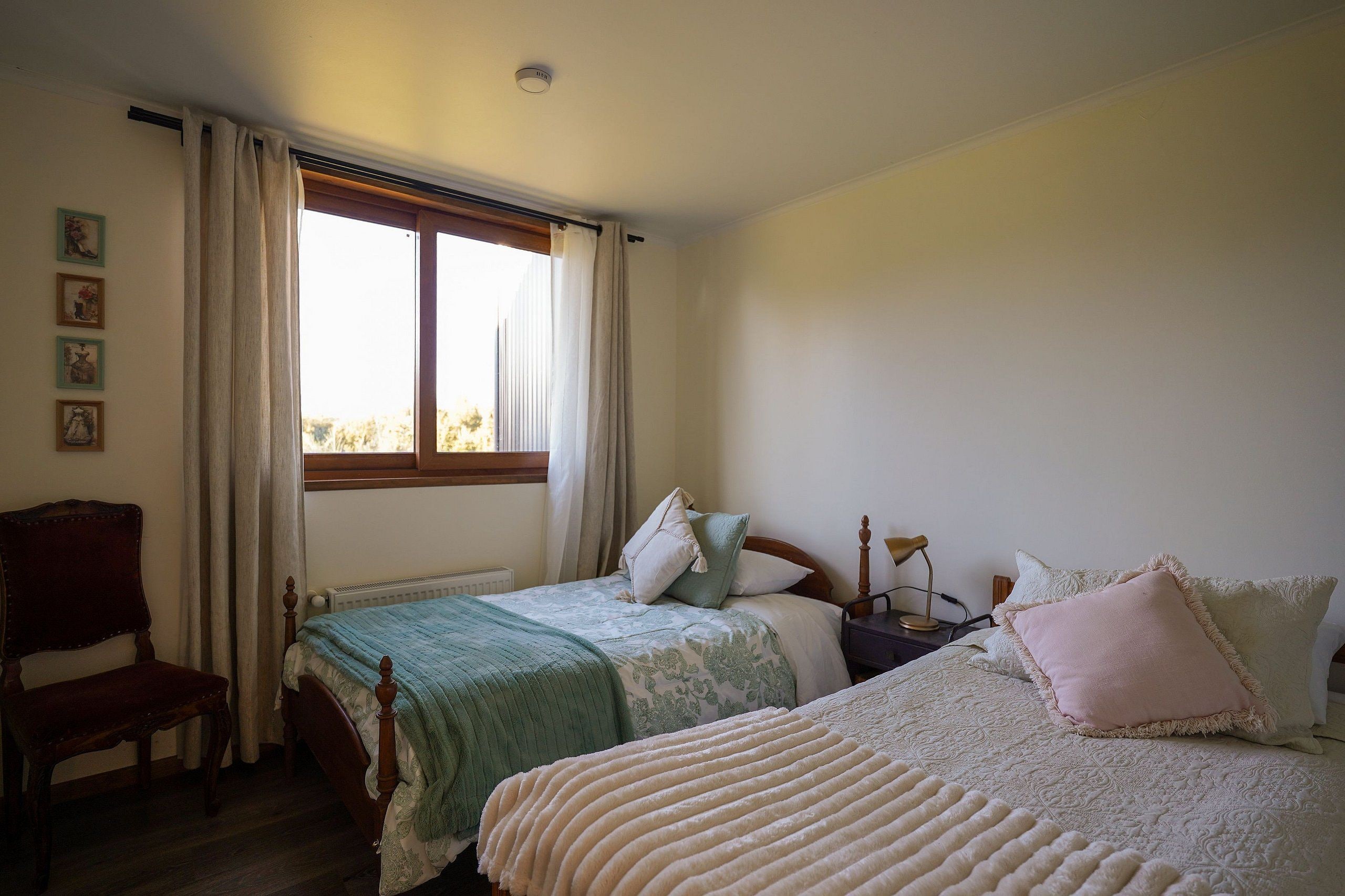 Een slaapkamer met twee bedden, een stoel, een bureau en een raam met gordijnen.