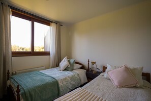 A bedroom with two beds, a window with curtains, a radiator, and a bedside lamp. - Oceana Suites Altos de Neoalerce (Puerto Montt)