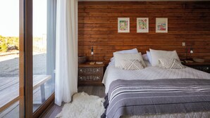 Une chambre à coucher avec une tête de lit en bois, un grand lit avec une literie blanche, une table de chevet avec une lampe et une vue par une fenêtre ornée de rideaux.