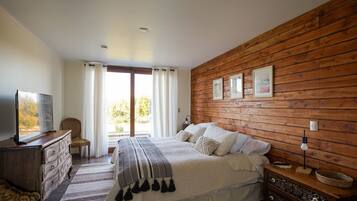 A bedroom with a wooden wall, a bed with white bedding, a television on a dresser, and a window with curtains.
