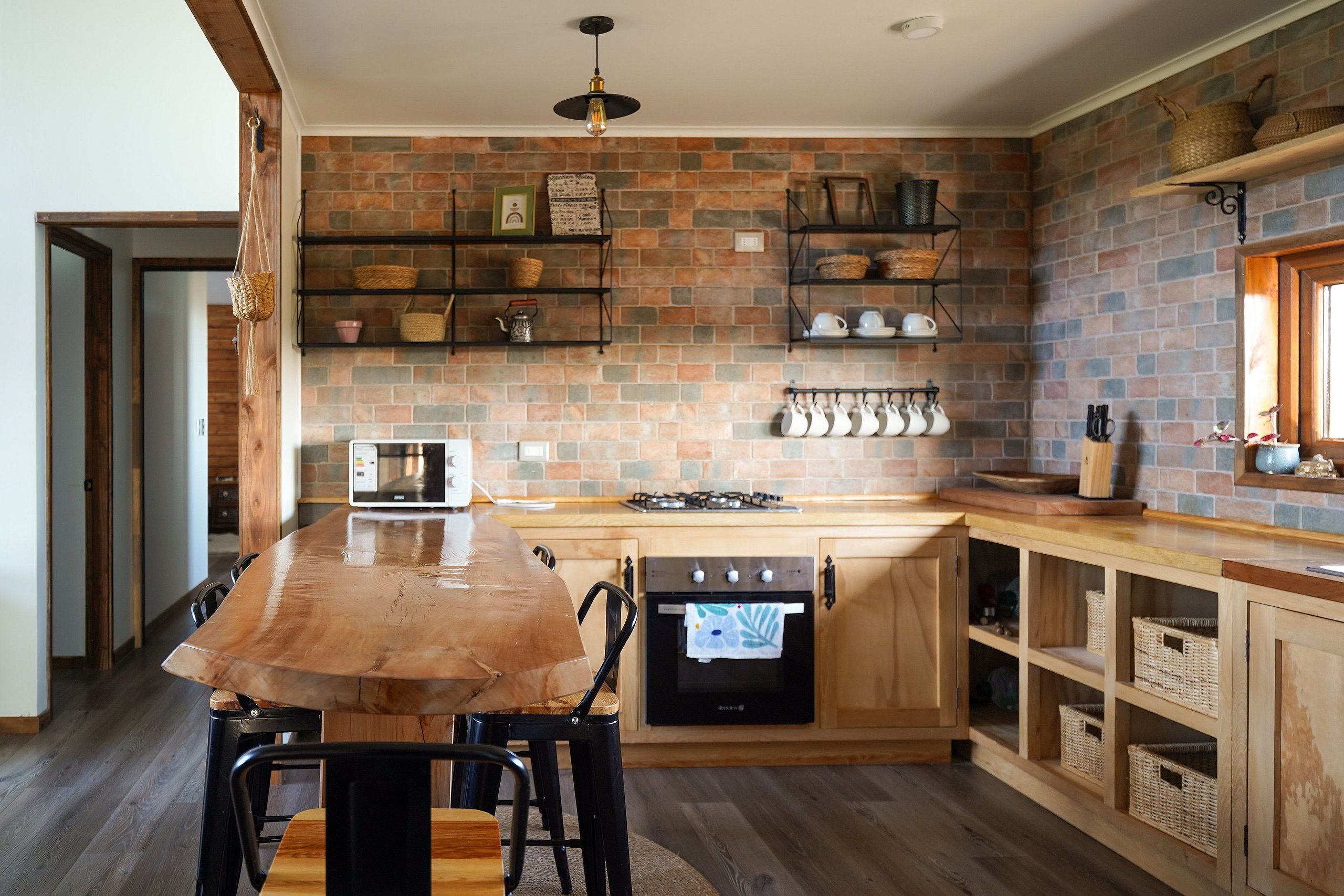 A kitchen with a brick backsplash, wooden cabinets, and a central island with chairs.