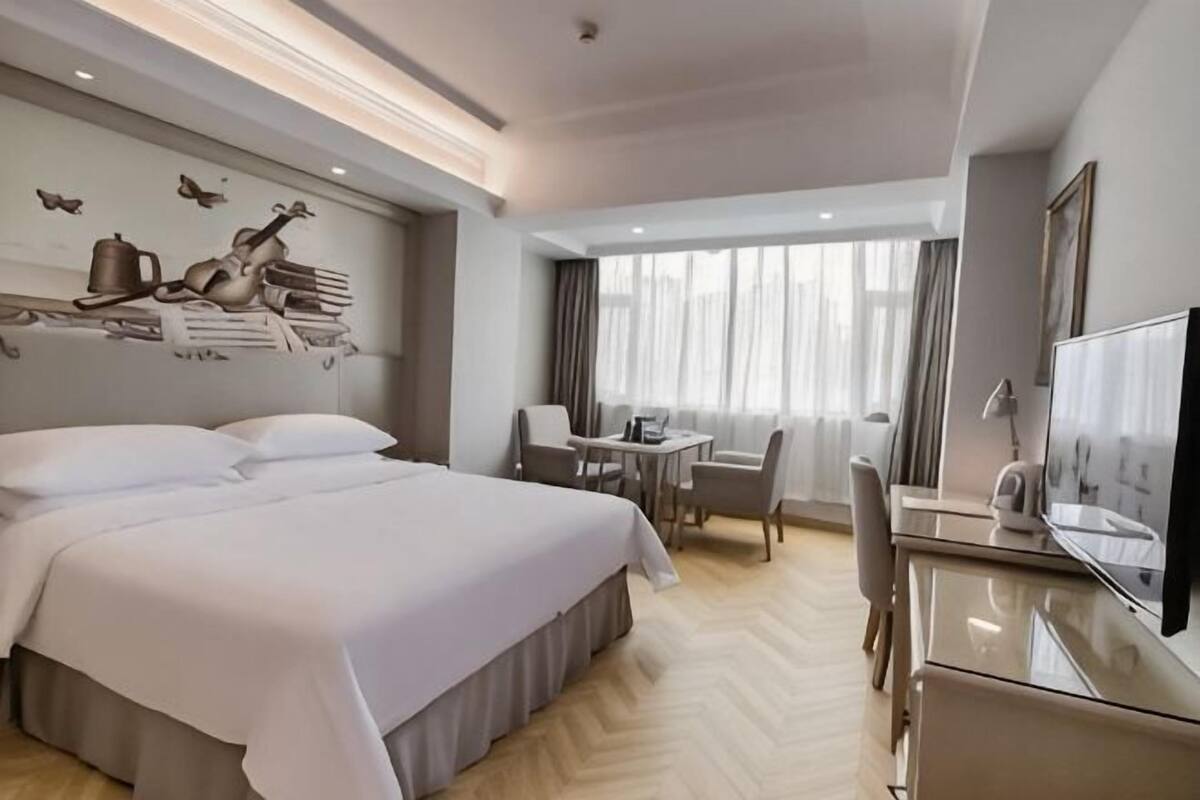 Ein Hotelzimmer mit einem großen Bett, einem Schreibtisch, einem Stuhl, einem Fernseher und einem Fenster mit Vorhängen.