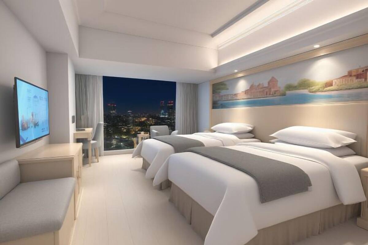A modern hotel room with a city view, a bed, a desk, and a TV.