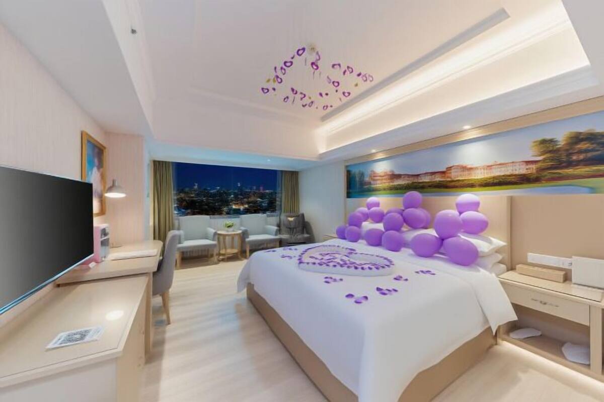 A modern hotel room with a large bed, a flat-screen TV, a desk, and a painting on the wall.
