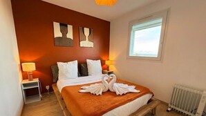A bedroom with a wooden bed, white bedding, a brown throw, and a window with a view. - Perle de Carnon Plage (Mauguio)