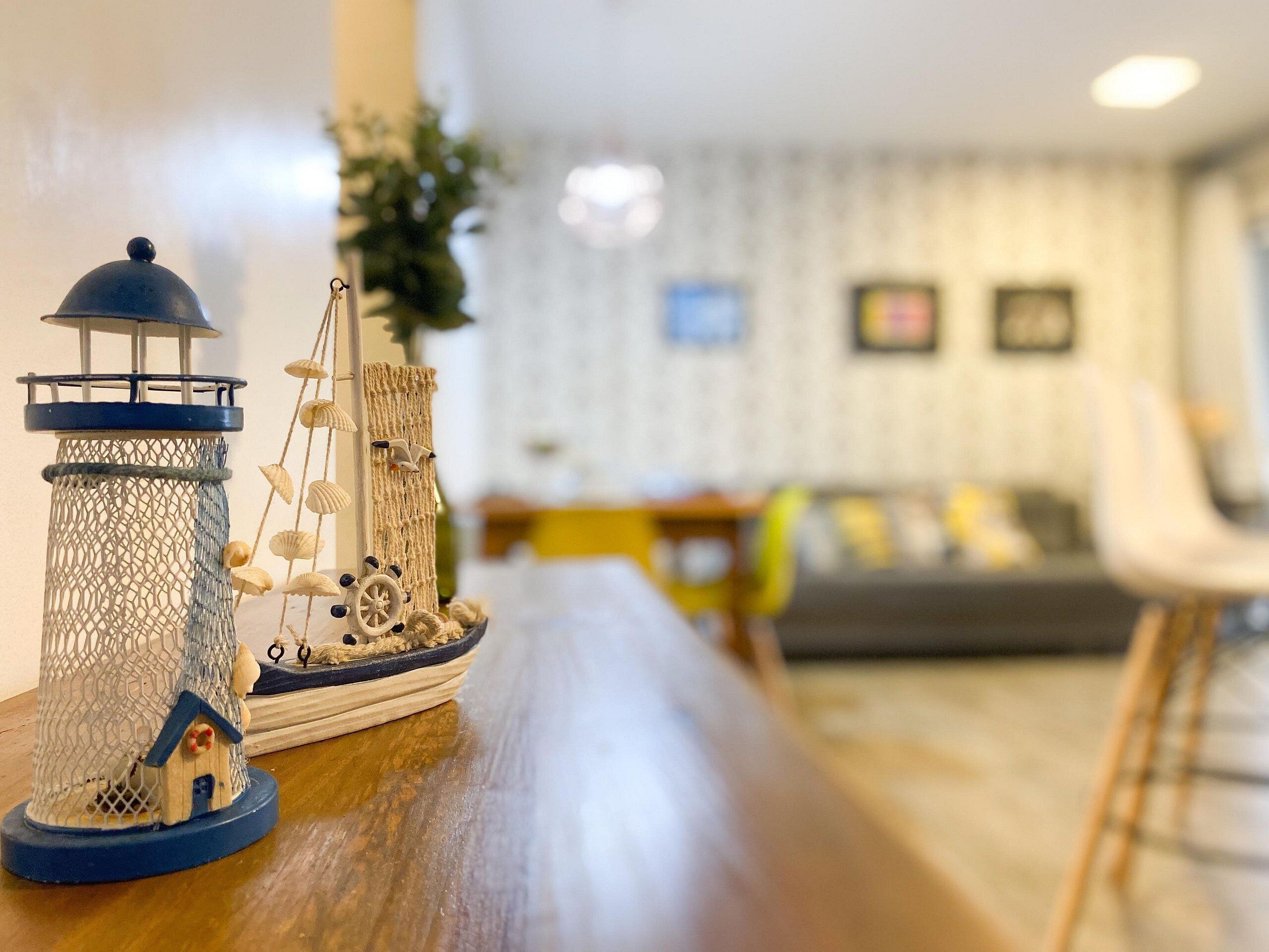 Ein Modellschiff mit Leuchtturm und Segelboot auf einer Holztischplatte.