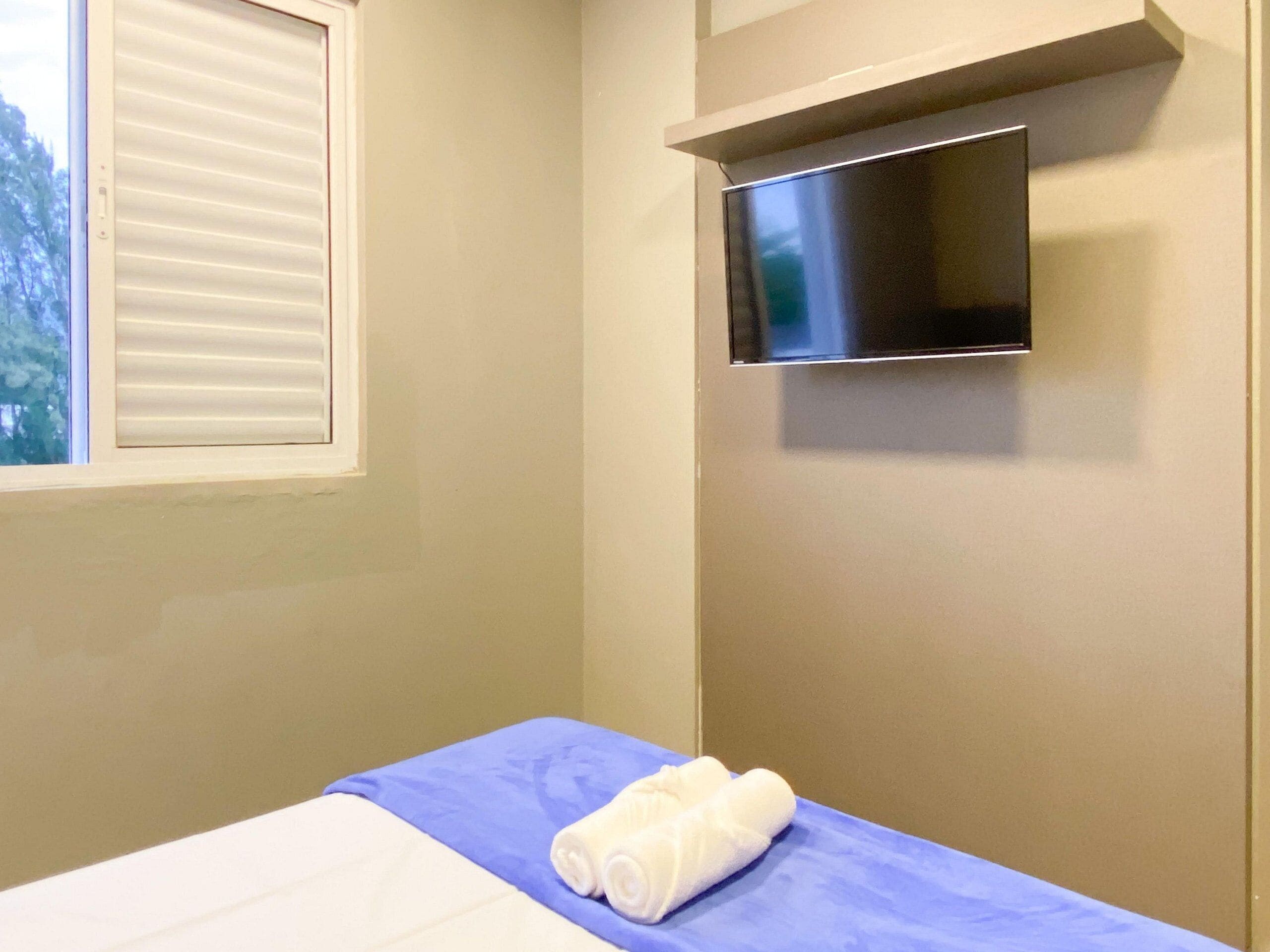 Una habitación de hotel con una cama, una ventana con persianas y un televisor de pantalla plana montado en la pared.