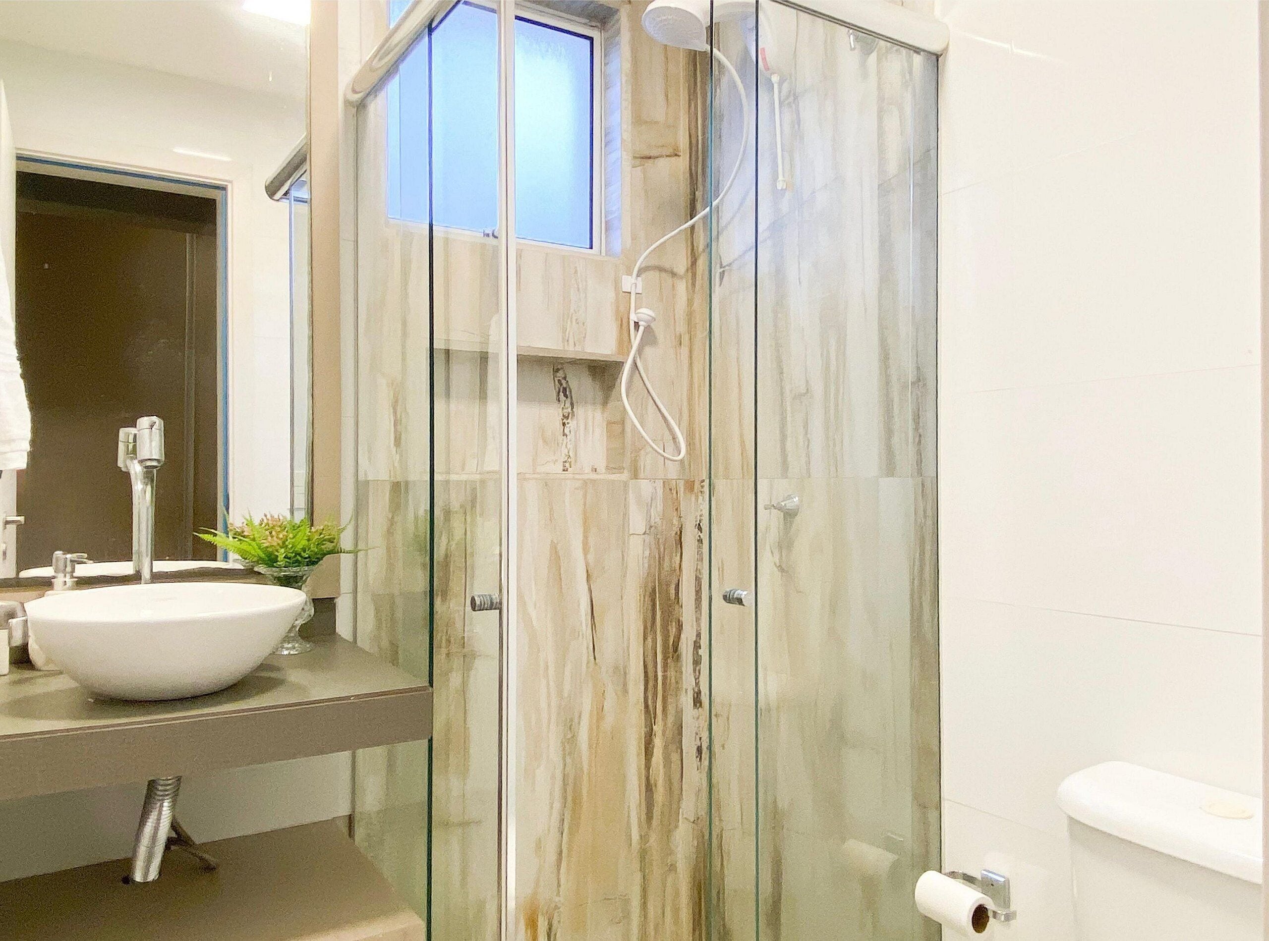 Un baño moderno con ducha de vidrio, un lavabo blanco y un inodoro.