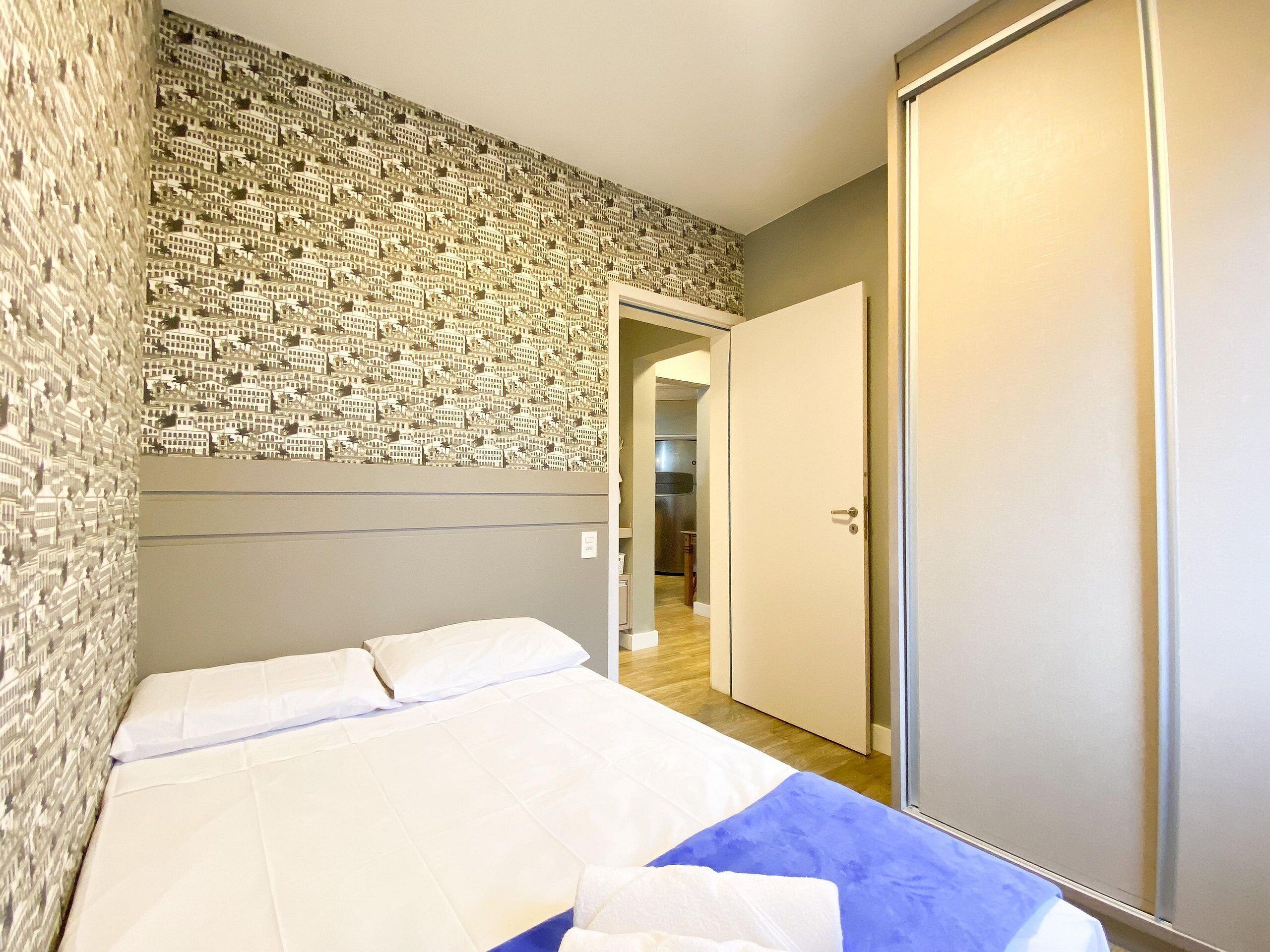 Quarto com cama, guarda-roupa e parede com papel de parede estampado.