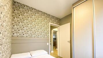 Quarto com cama, guarda-roupa e parede com papel de parede estampado.