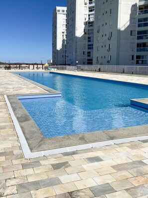 A rectangular swimming pool with a tiled edge, surrounded by a stone deck. - Resid. Clube Mar Grosso-Laguna - LAG208 (Laguna)