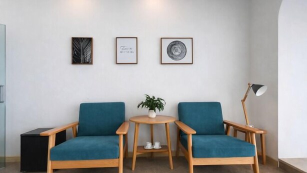 A room with two blue chairs, a small round wooden table with a plant, and two framed artworks on the wall. - Heceng Qiyuan Art Hotel (Dali City)
