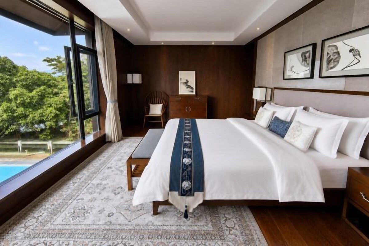 A bedroom with a large bed, a view of a swimming pool, and a wooden headboard.