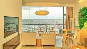 Un salon moderne doté d’une grande fenêtre donnant sur la mer, un coin repas avec des meubles en bois et un mur décoré de plantes.