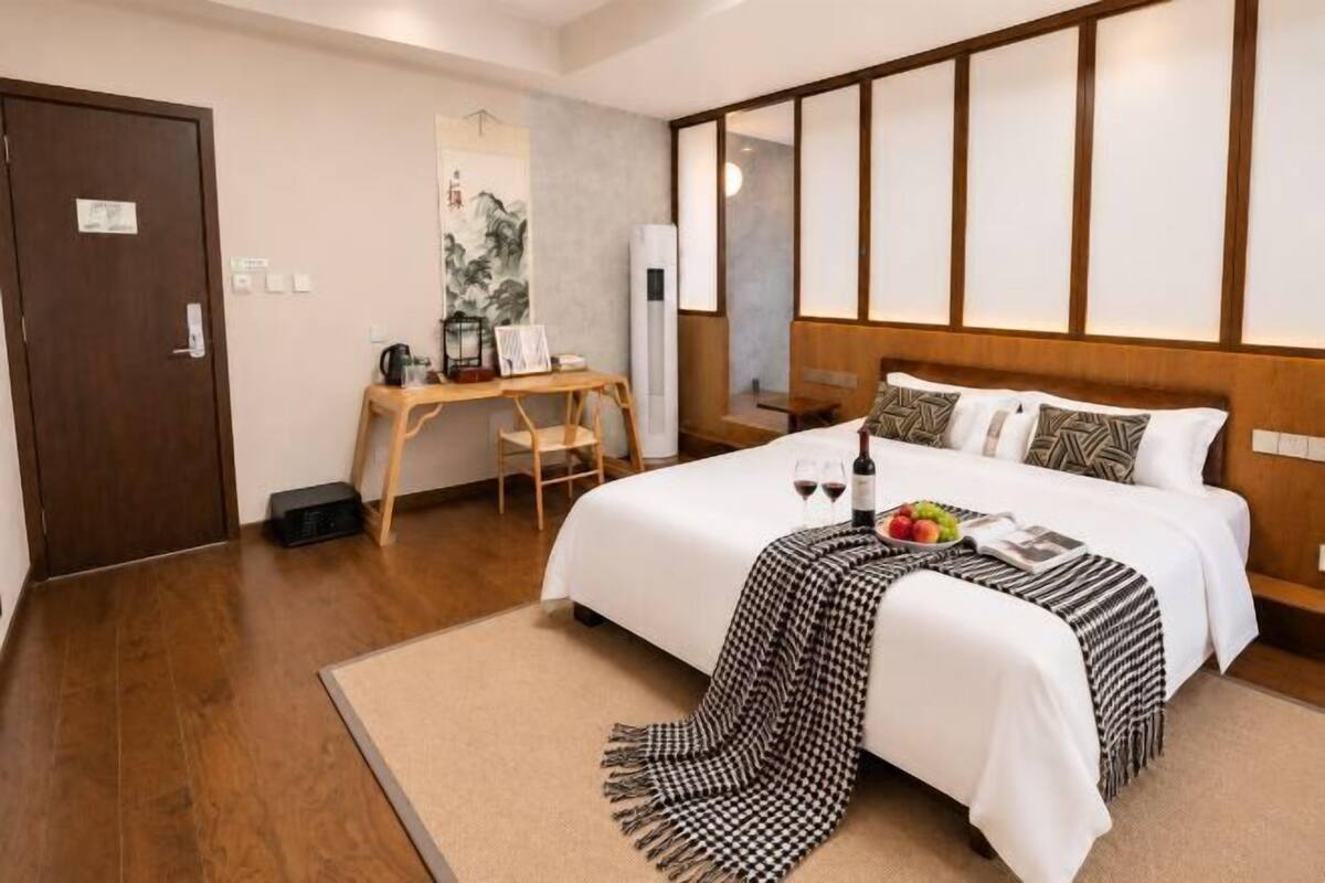 A hotel room with a bed, bedside table, desk, chair, and a large mirror.