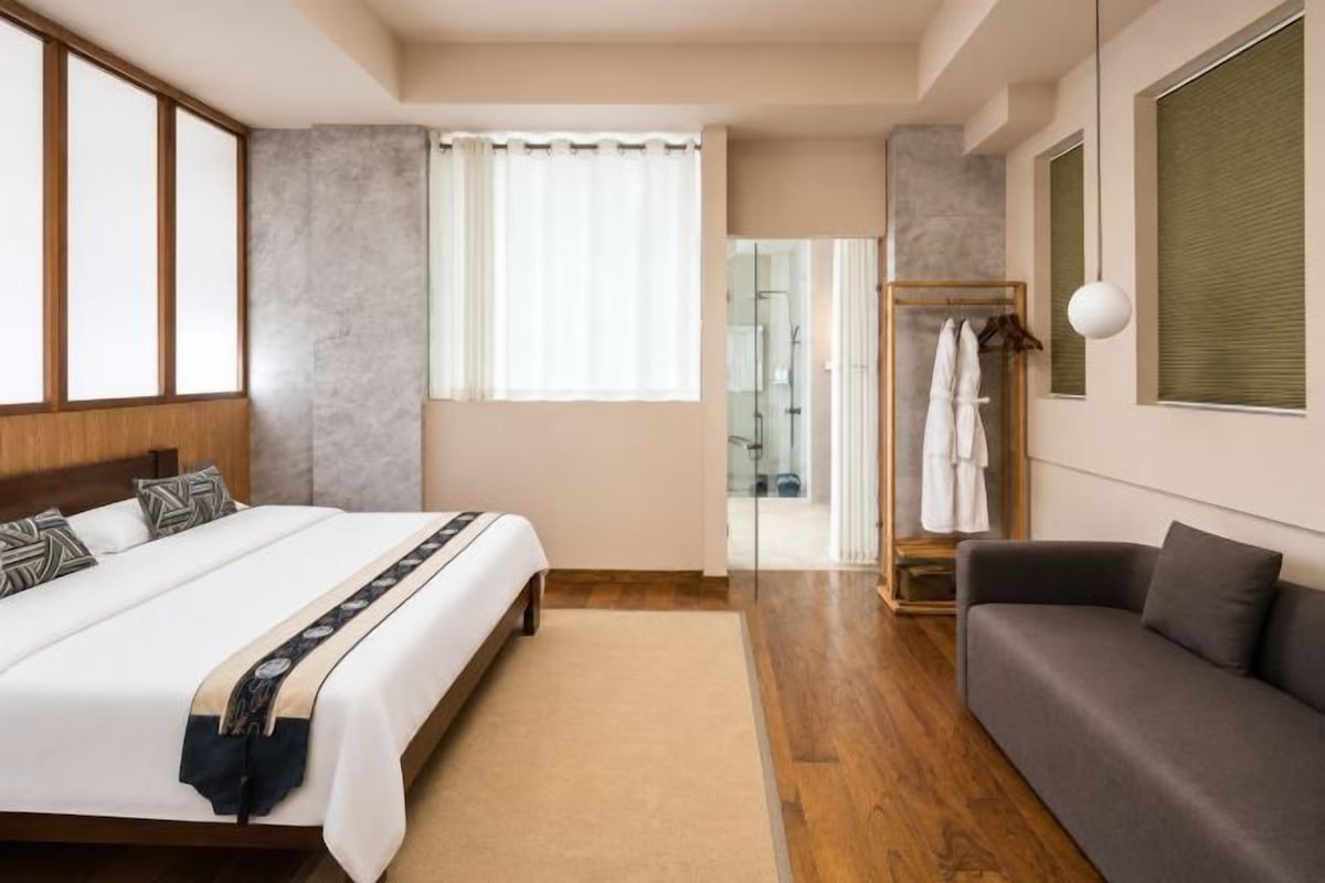 A hotel room with a bed, a sofa, a walk-in closet, and a bathroom with a glass door.