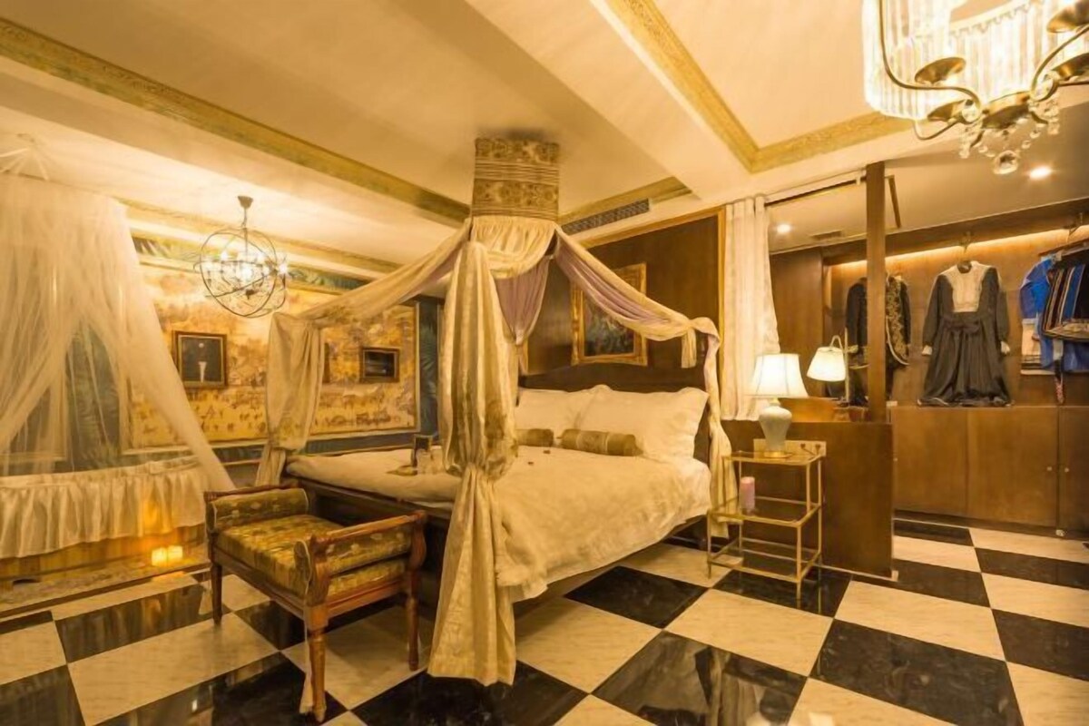 A luxurious bedroom with a four-poster bed, a sitting area, and a vanity with clothing.