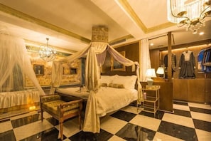 A luxurious bedroom with a four-poster bed, a sitting area, and a vanity with clothing.