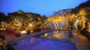 Un espace extérieur avec piscine, aménagé pour la nuit, avec des arbres et des éclairages.