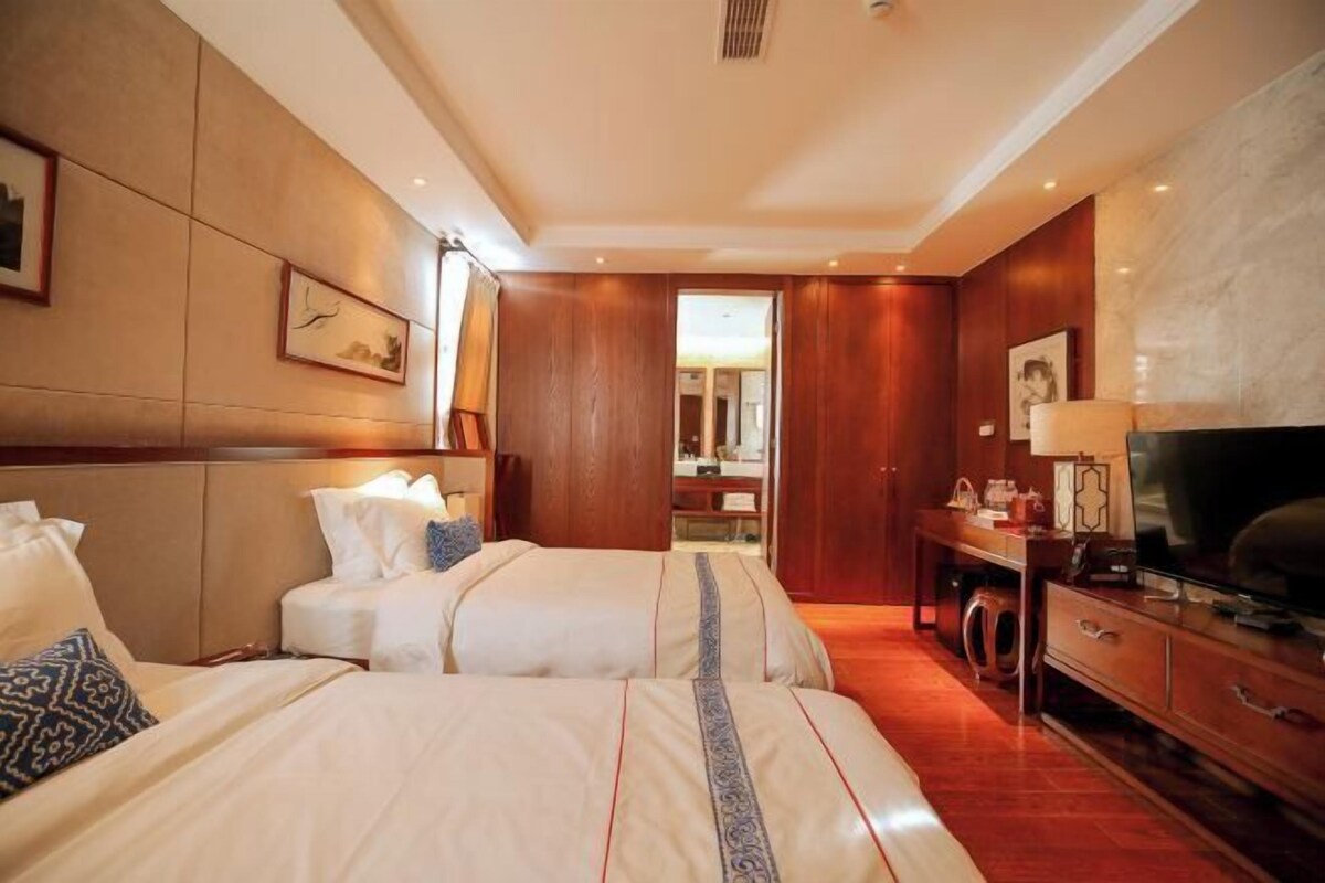 A hotel room with two beds, a TV, a desk, and a mirror.