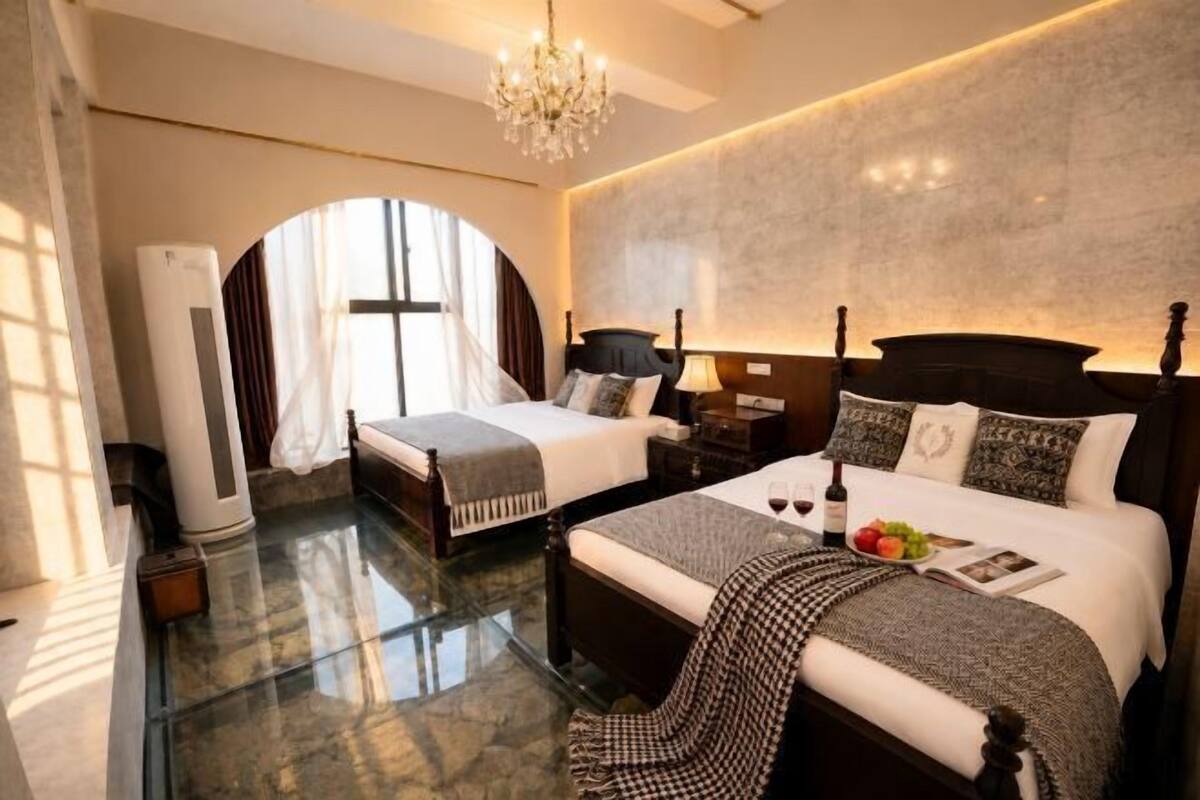 A hotel room with two beds, a chandelier, a large window with curtains, and a marble floor.