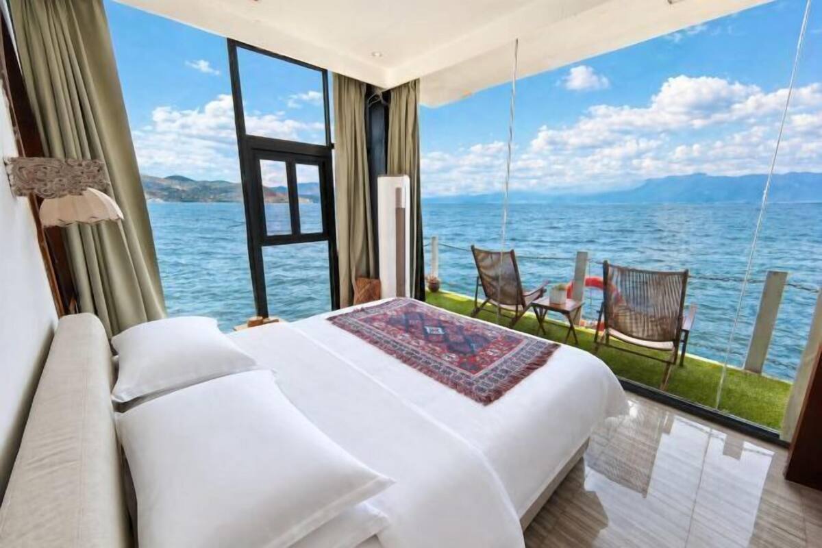 A bedroom with a large bed, a view of the sea, and a balcony with chairs.