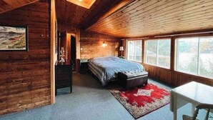 A cozy wooden cabin bedroom with a bed, a small table, and a window.