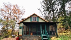 A rustic cabin with a porch, surrounded by trees and fallen leaves.