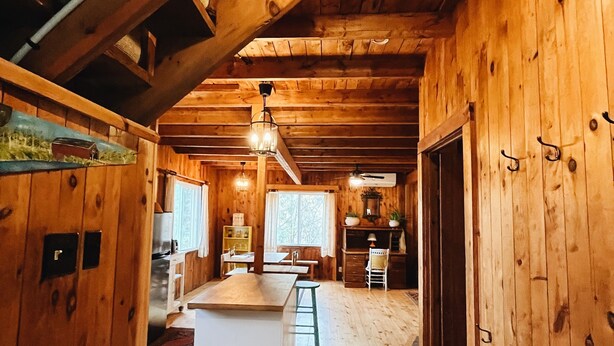 A wooden cabin interior with a central island, wooden floors, and a ceiling with exposed beams.