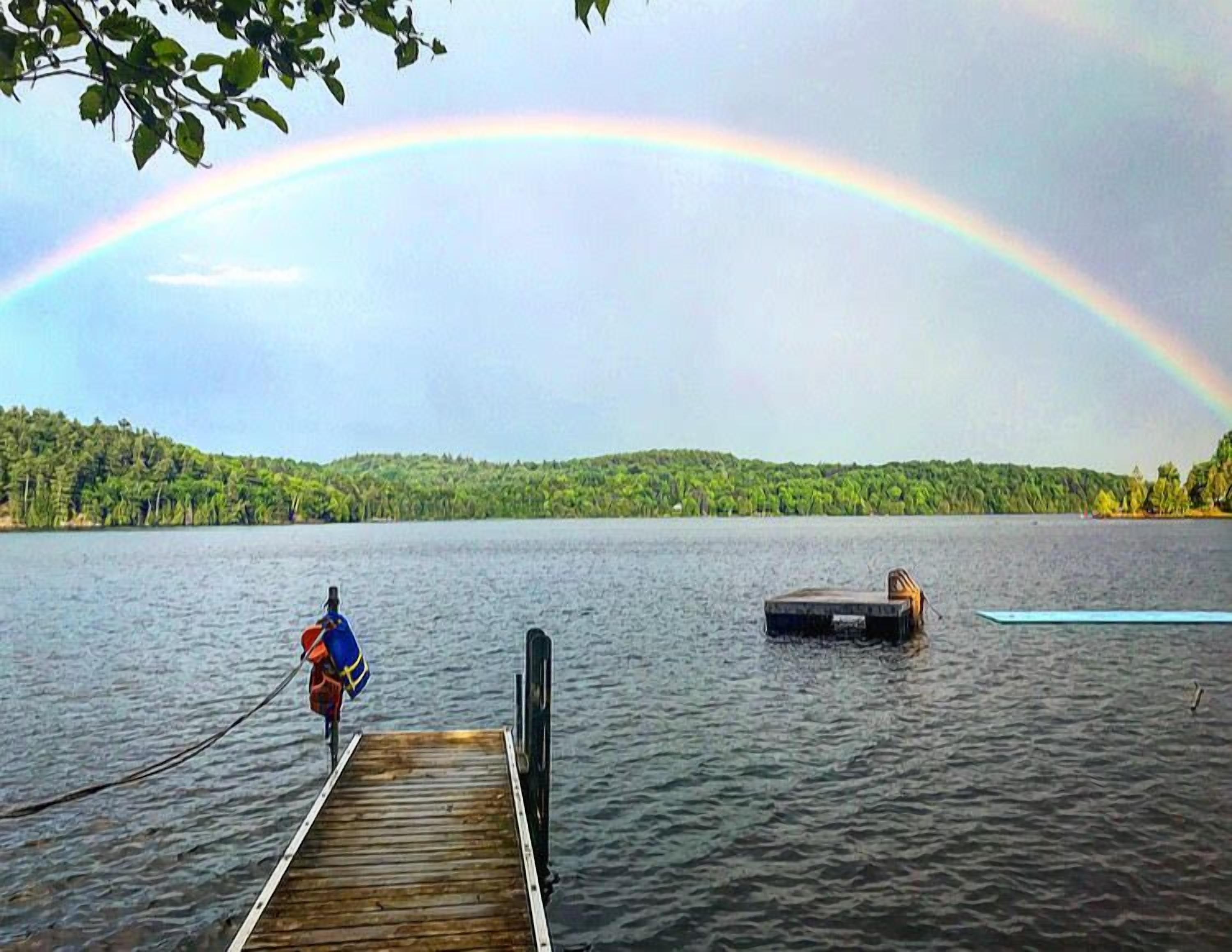 Eine Holzstege führt in einen See, im Hintergrund ein Regenbogen.