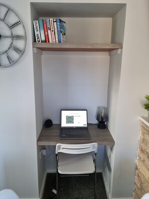 A compact workspace with a laptop, books, a clock, and a small plant.