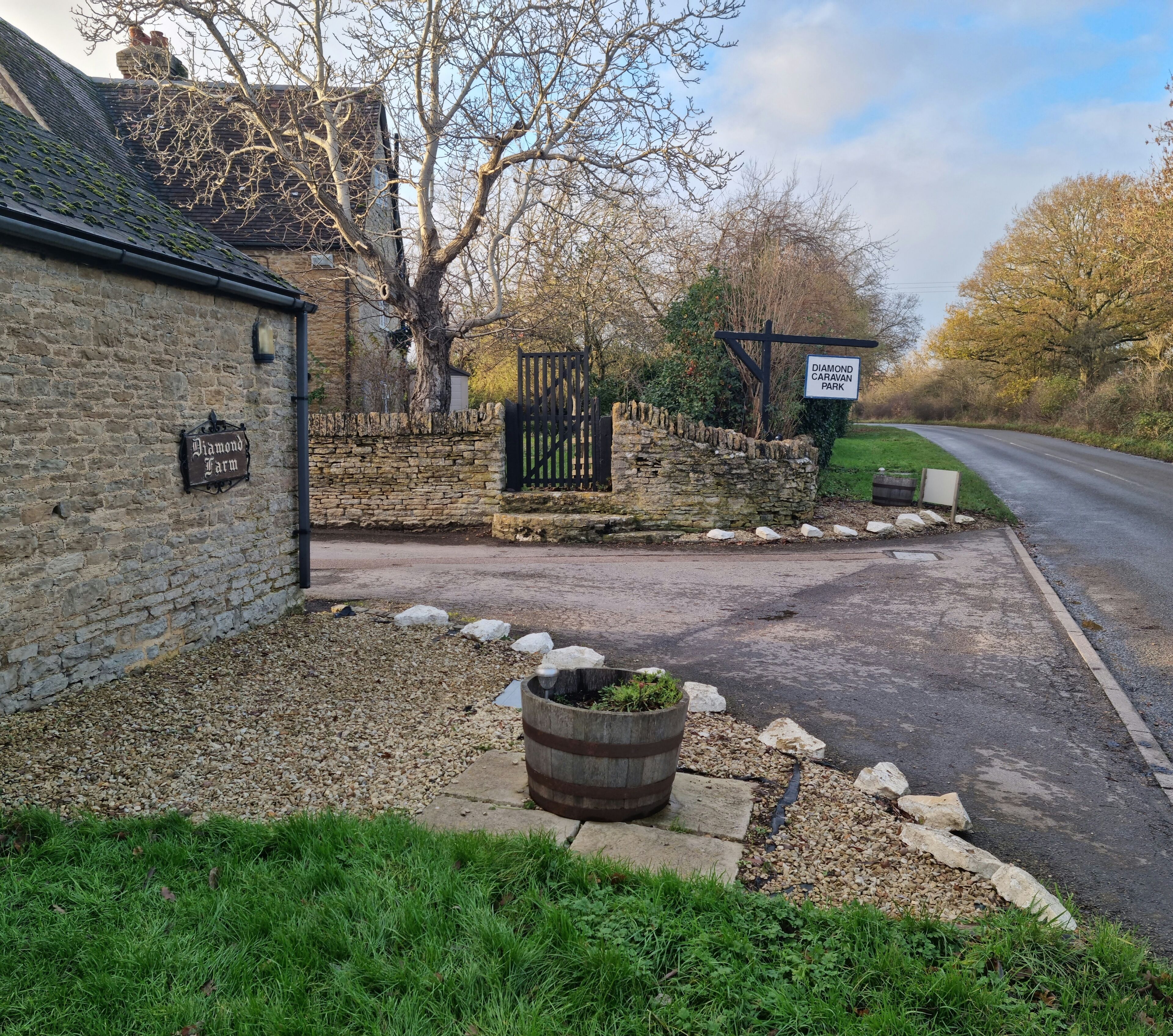 A rural setting with a stone wall, a sign for 'Diamond Farm,' a gated entrance, and a road leading to a park.. Cosy two bedroom countryside apartment. Close to major attractions. Dog Friendly