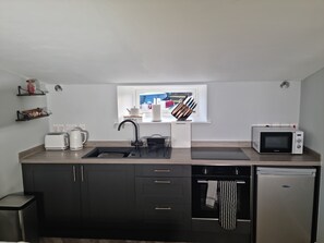 A modern kitchen with a sink, toaster, kettle, microwave, and a refrigerator.