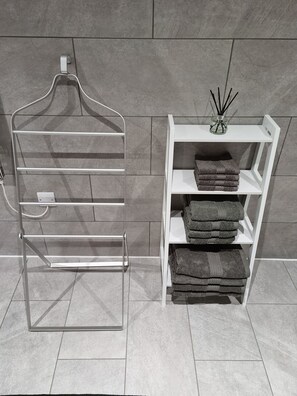 A bathroom with a towel rack and a shelf with folded towels and a reed diffuser.