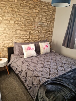 Ein Zimmer mit Steinwand, einem Bett mit grauer Decke und zwei Kissen mit Flamingos.