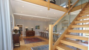 A spacious living area with a wooden staircase, a dining table set for four, and a large painting on the wall. - Drackenorth (Beaminster)