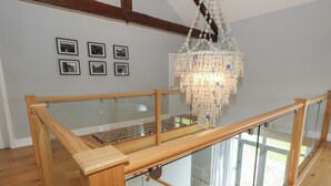 A spacious room with a wooden staircase, a glass railing, and a chandelier. - Drackenorth (Beaminster)