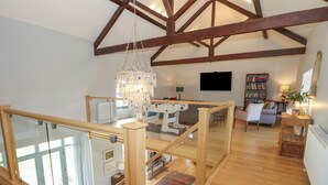 A spacious loft with high ceilings, exposed wooden beams, a glass railing, a chandelier, a television, a bookshelf, and a cozy seating area. - Drackenorth (Beaminster)