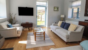 A living room with a sofa, a coffee table, and a TV mounted on the wall. - Tothery (Beaminster)