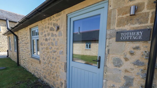 A stone cottage with a blue door and a sign reading "TOOTHERY COTTAGE." - Tothery (Beaminster)