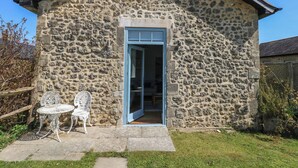 A stone building with a blue door and a small patio with two white metal chairs. - Tothery (Beaminster)