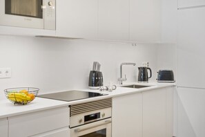 Et moderne køkken med hvide skabe, en stålvask, en Bosch mikrobølgeovn, en brødrister og en elkedel.