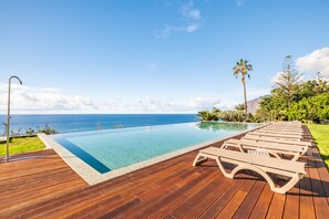 A wooden deck with a pool and lounge chairs overlooking the ocean.
