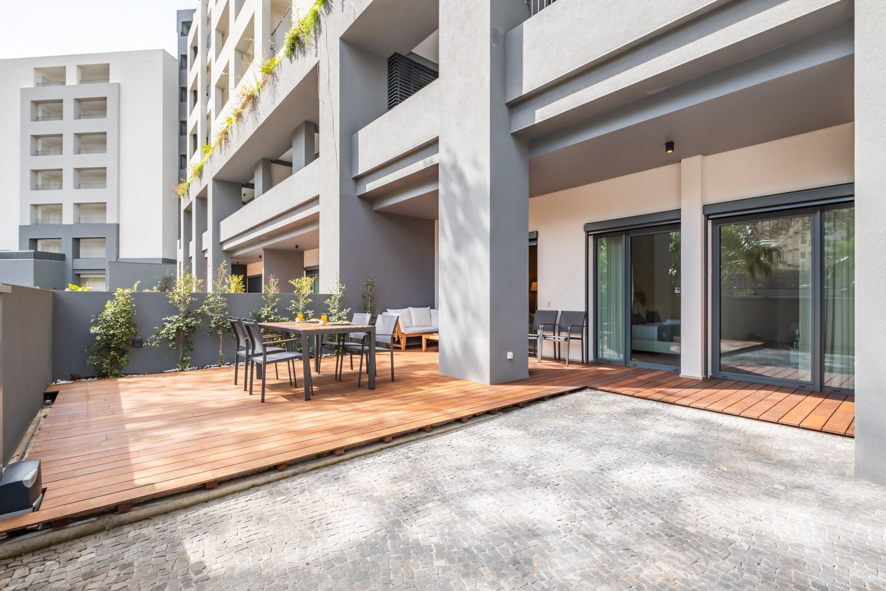 A modern outdoor patio with a wooden deck, seating area, and a view of a building with balconies.