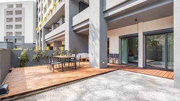 A modern outdoor patio with a wooden deck, seating area, and a view of a building with balconies.