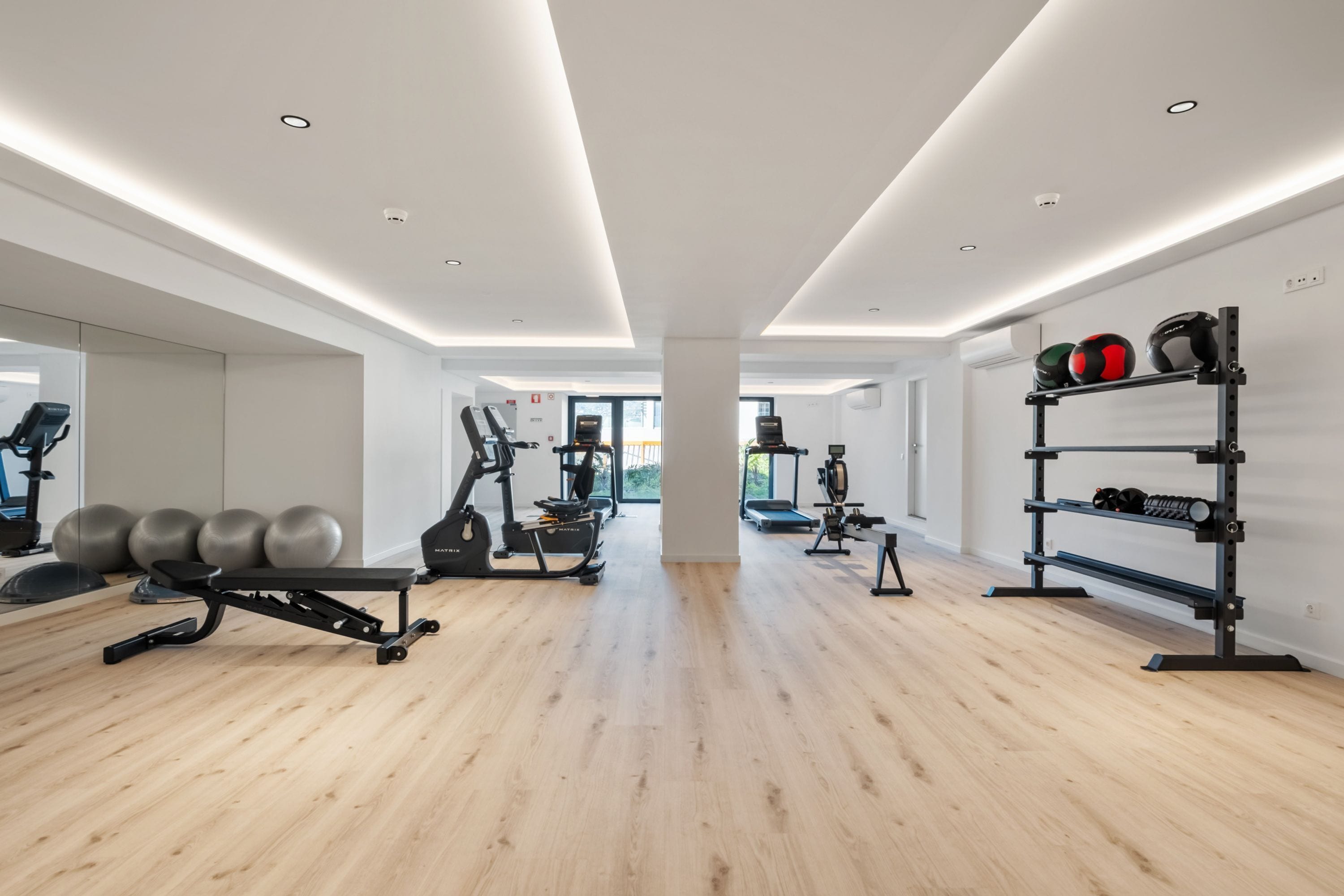 Ein modernes Fitnessstudio mit Trainingsgeräten, Holzboden und einem großen Fenster.