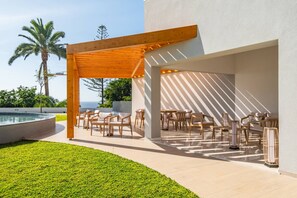 Eine Terrasse im Freien mit Holzmöbeln und einem Pool, umgeben von einem gepflegten Rasen und Palmen.