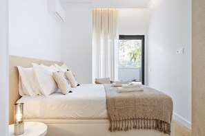 Una habitación de hotel moderna con una cama grande, una mesita de noche con una lámpara y vistas al exterior a través de una ventana con cortinas.
